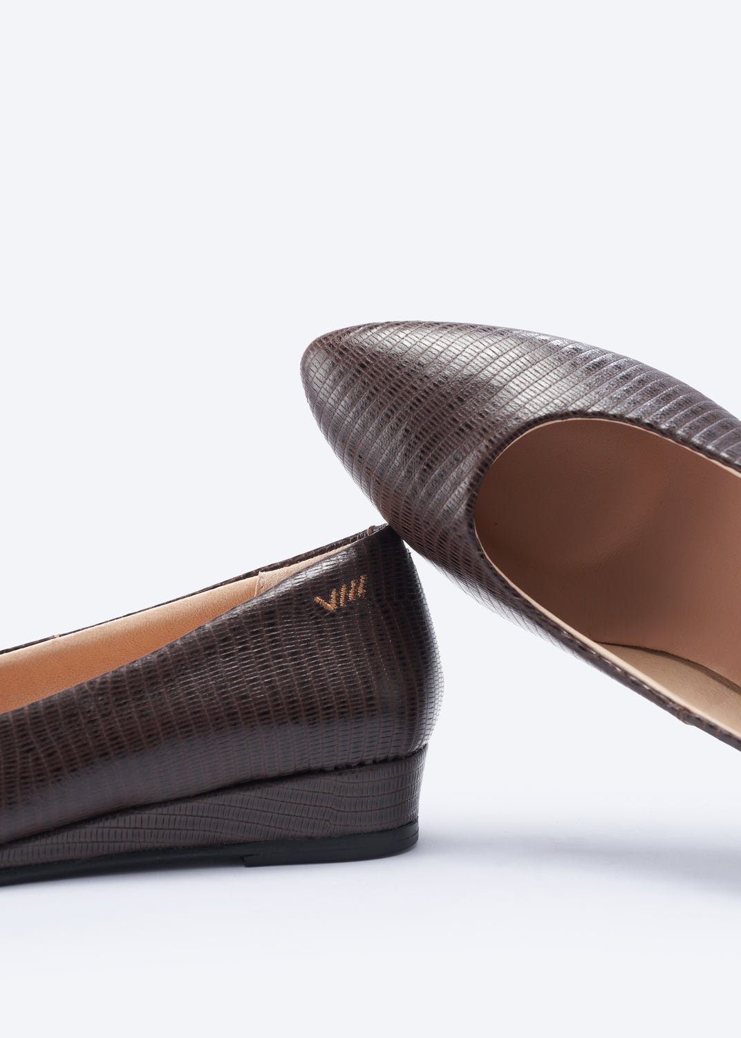 A close-up studio shot of a pair of women's wedge flats in dark brown textured leather, showing the pointed toe and interior lining on a clean white background.
