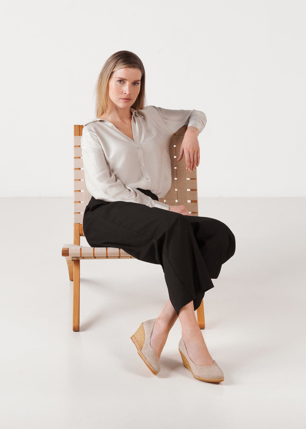 Model seated in studio wearing Roses gold canvas slip-on wedge espadrilles, full-body view with crossed legs.