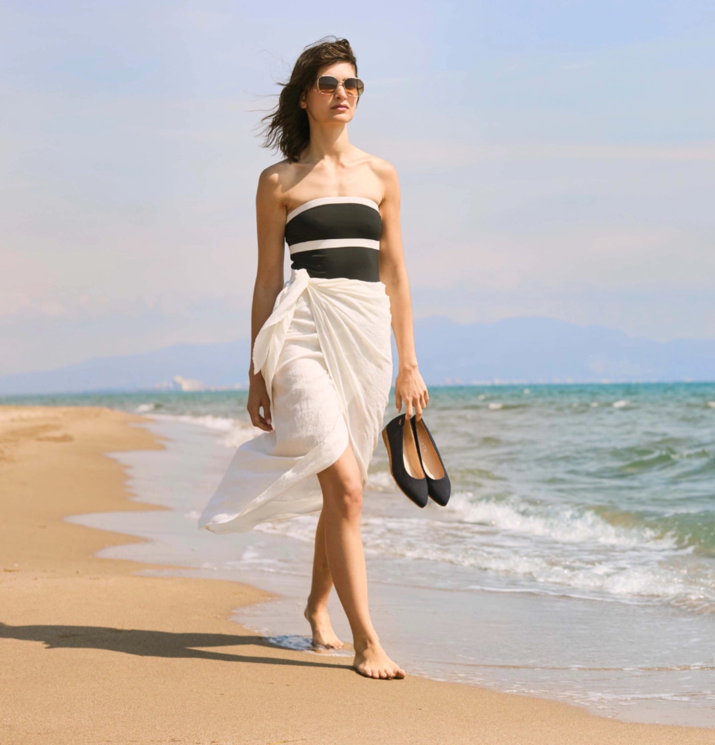 Woman in a black and white dress walking on a beach with ocean and sky in the background