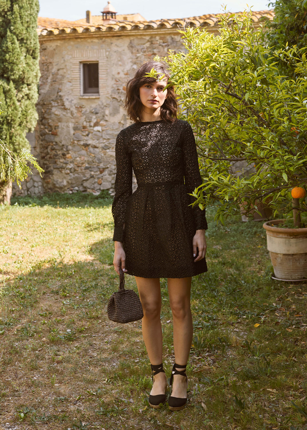 Woman wearing black lace-up wedge espadrilles styled with a black dress in a Mediterranean garden setting.