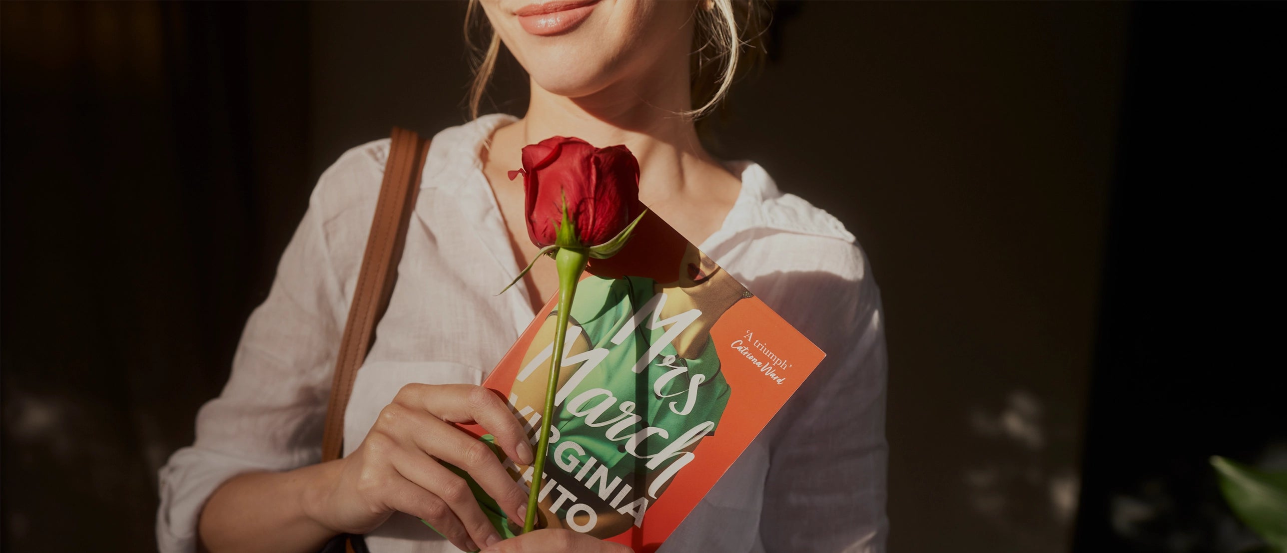 Woman in white blouse holding a red rose and the novel 'Mrs. March' by Virginia Feito, bathed in warm natural light with a soft smile, evoking elegance and literary charm