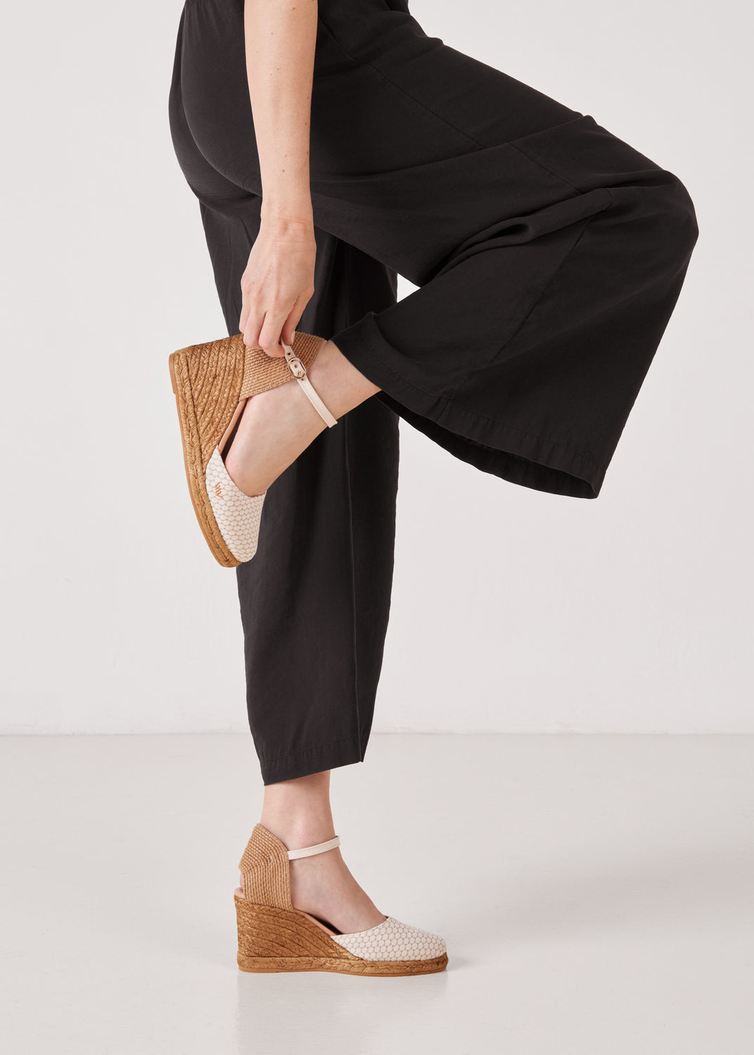 Women’s white mesh-canvas ankle-strap wedge espadrilles with jute platform, styled with black wide-leg pants in a clean studio setting.