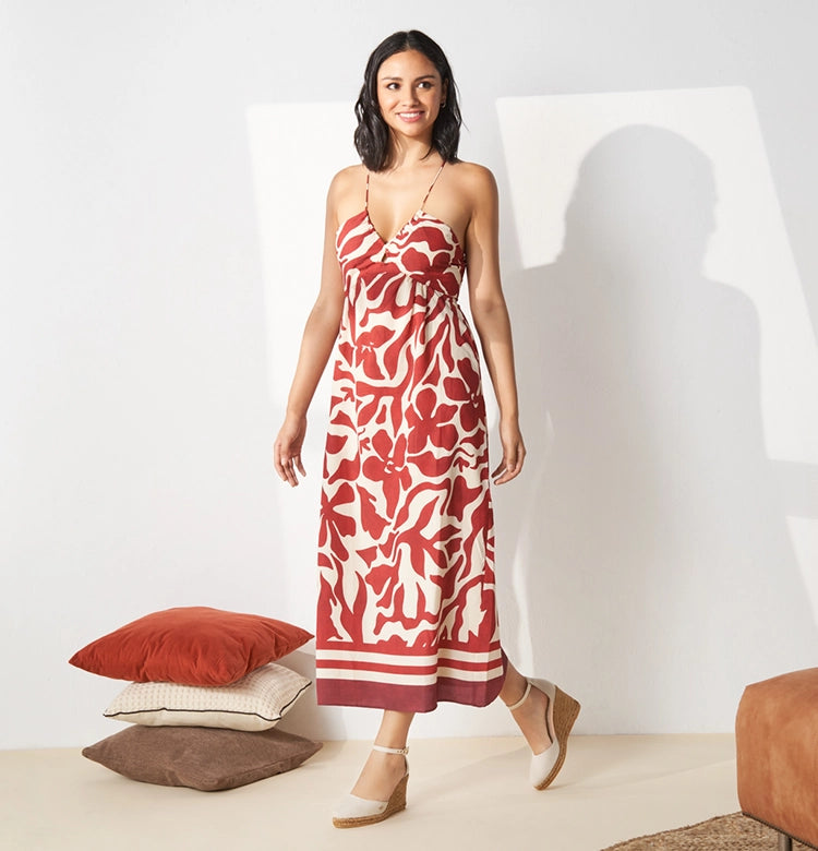 Woman in a red and cream tropical print sundress walking confidently indoors, styled with beige ankle-strap high wedge espadrilles — a fresh, feminine look ideal for summer parties, beach vacations, or effortless warm-weather style.