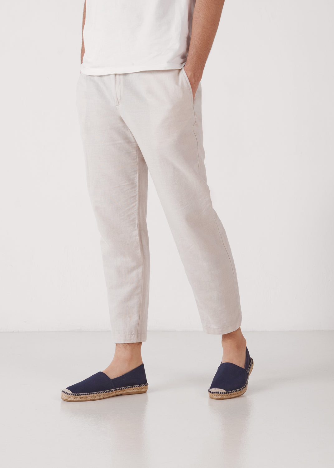 Men’s navy-blue canvas slip-on espadrilles with jute sole, styled with light linen trousers in a minimalist studio shot.