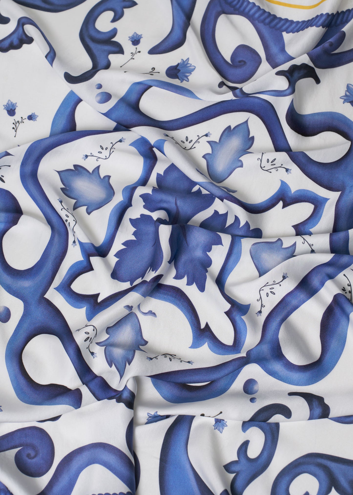Close-up of flowing carré scarf with deep blue baroque-style floral and scroll design on white background – elegant Mediterranean-inspired accessory highlighting smooth texture and artistic detail