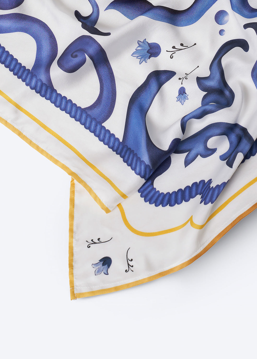 Close-up of square scarf corner with intricate cobalt blue scrollwork, delicate floral accents, and golden yellow border – premium accessory inspired by Mediterranean ceramic artistry