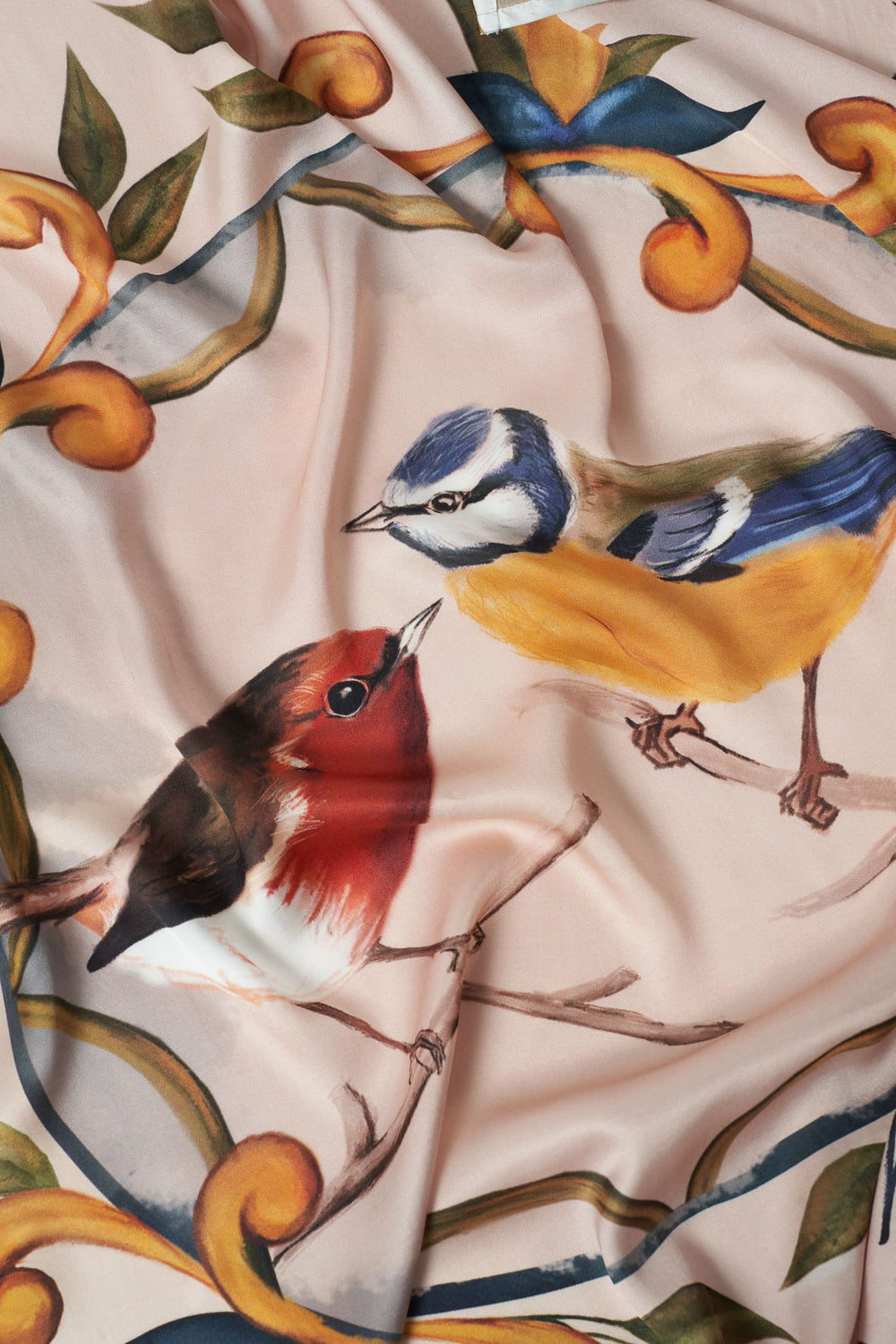 Detailed close-up of hand-painted red robin and blue tit birds on luxurious square scarf, featuring soft blush background and ornate botanical scroll design – artisanal accessory with nature-inspired elegance