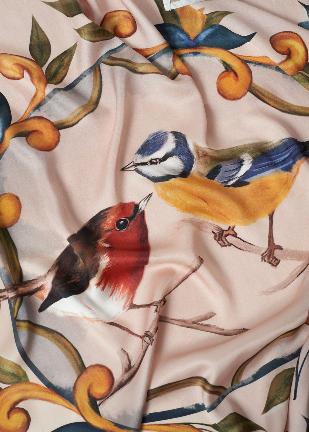Detailed close-up of hand-painted red robin and blue tit birds on luxurious square scarf, featuring soft blush background and ornate botanical scroll design – artisanal accessory with nature-inspired elegance