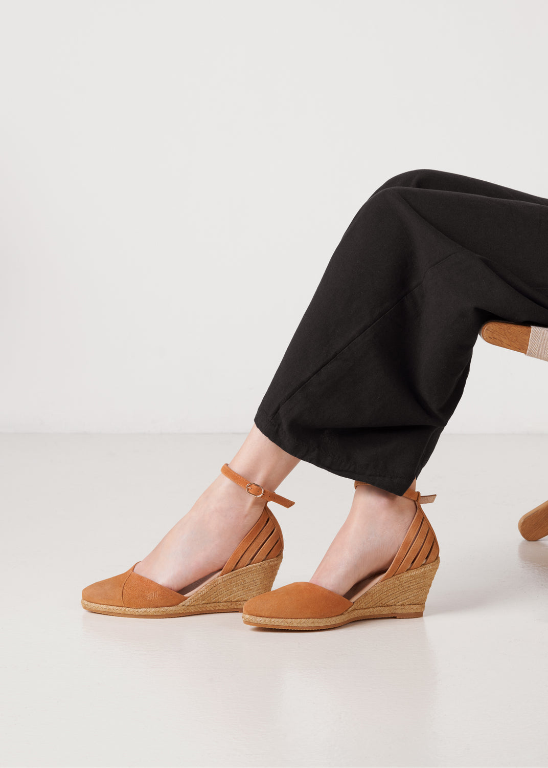 Close-up of camel suede ankle-strap wedge espadrilles with braided jute heel on model.