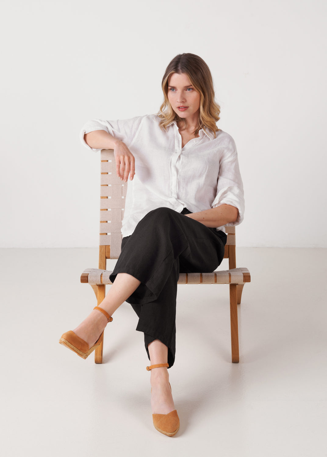 Model seated wearing camel suede ankle-strap wedge espadrilles with braided jute wedge in studio.