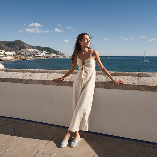 Woman enjoying the mediterranean sun wearing a beige linen jumpsuit paired with Barceloneta recycled canvas waves flat espadrilles