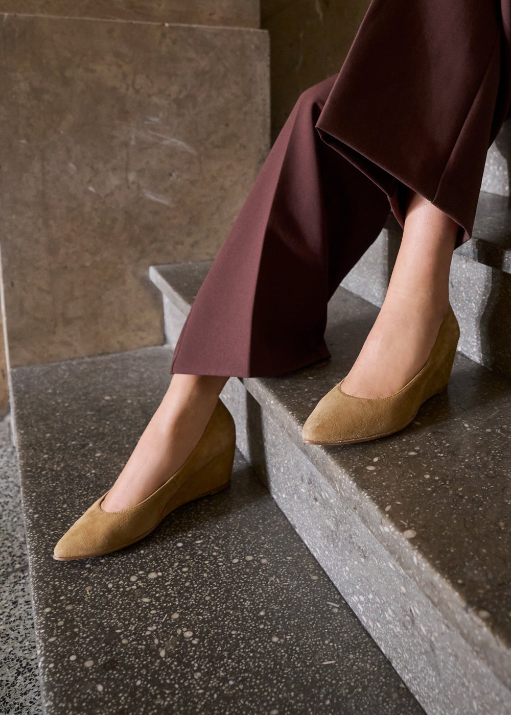 Close-up of woman wearing camel suede wedge shoes paired with brown wide-leg trousers — Viscata Essenza collection, classic comfort meets style.