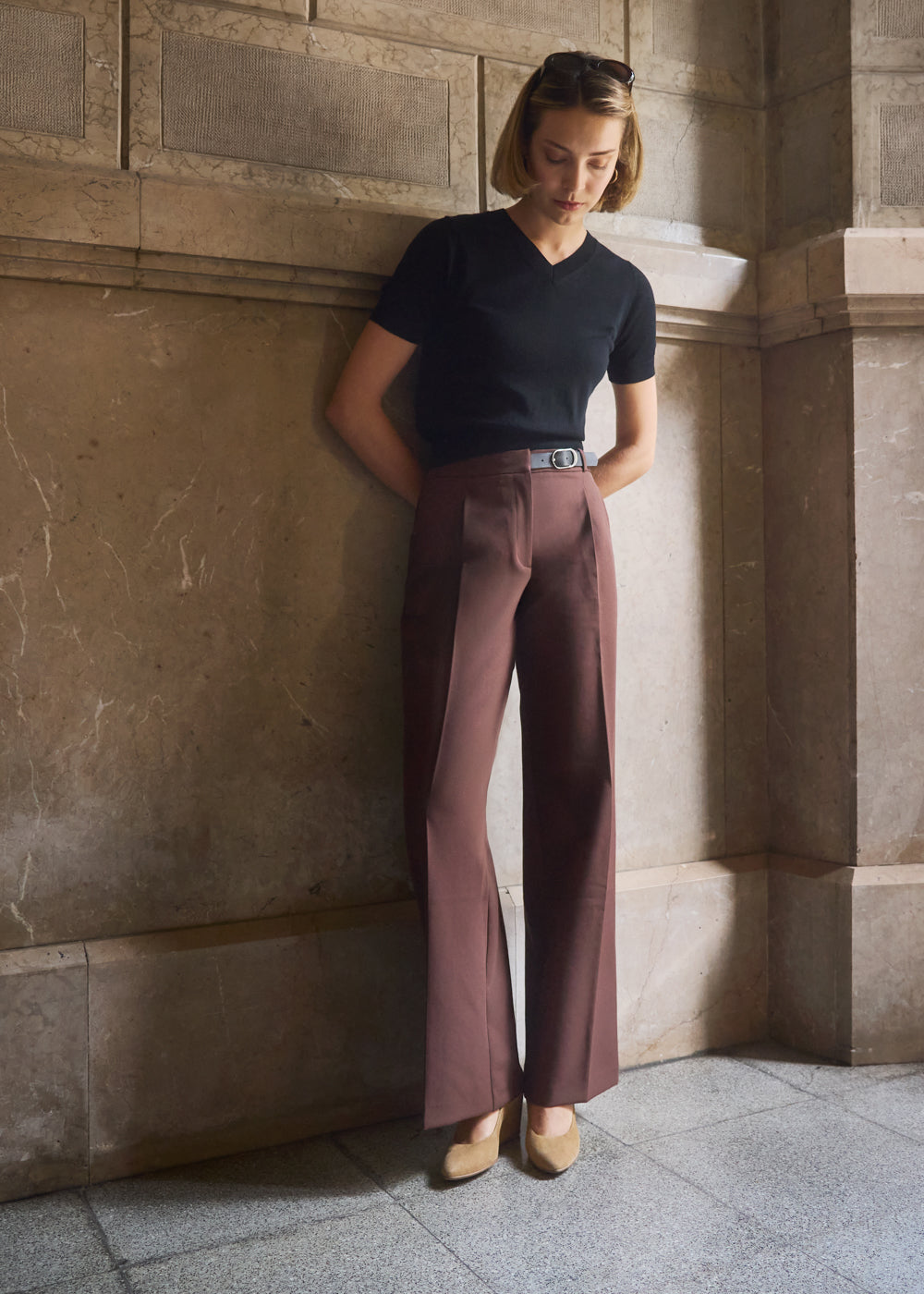 Woman in a minimalist setting wearing a black top and brown tailored trousers styled with camel suede wedge shoes — Viscata Essenza collection, modern elegance for everyday wear.
