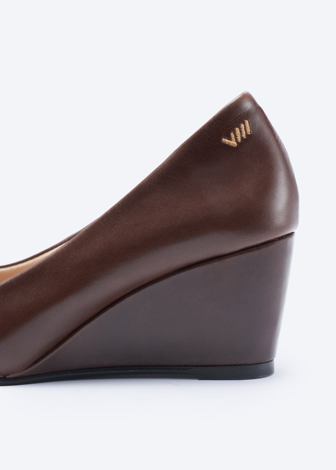A close-up side view of a dark brown leather wedge pump shoe with a small gold logo on the heel, set against a clean white background.