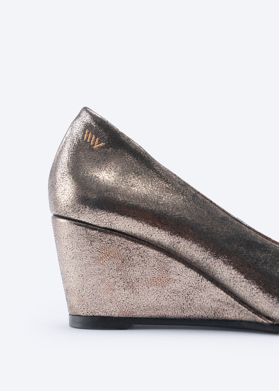Close-up side view of a metallic wedge pump shoe in a champagne gold finish, showing the side profile, heel, and a small gold logo on the heel counter.