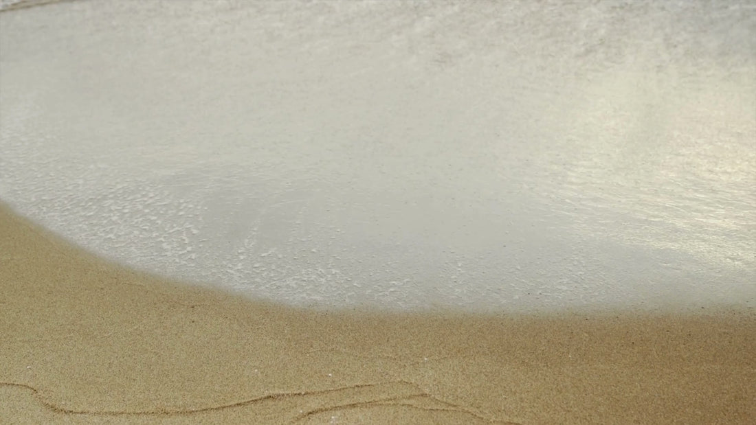 Gentle ocean waves roll onto a sandy beach, with white foam washing in and receding in a steady rhythm.